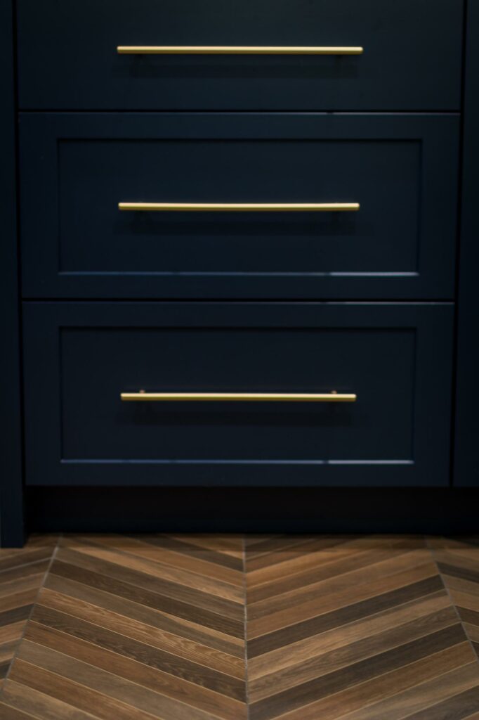 Black modern cabinet with brass handles, herringbone wood floor.