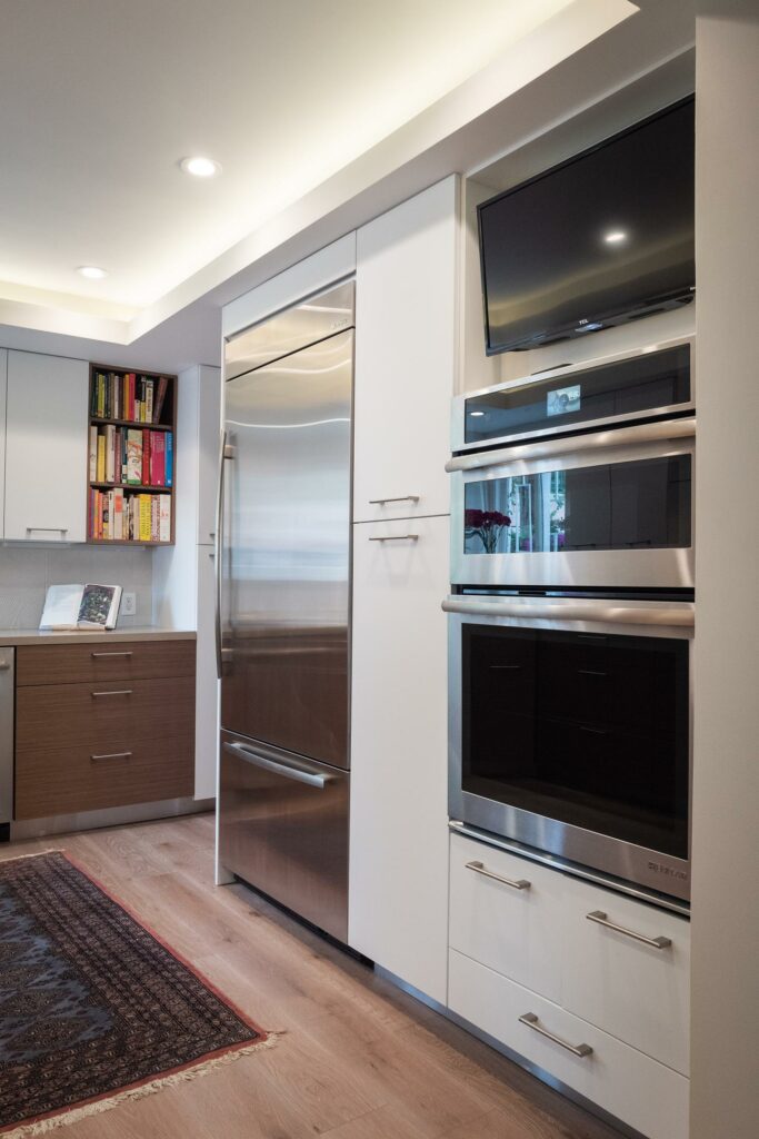 Modern kitchen with stainless steel appliances and bookshelf.