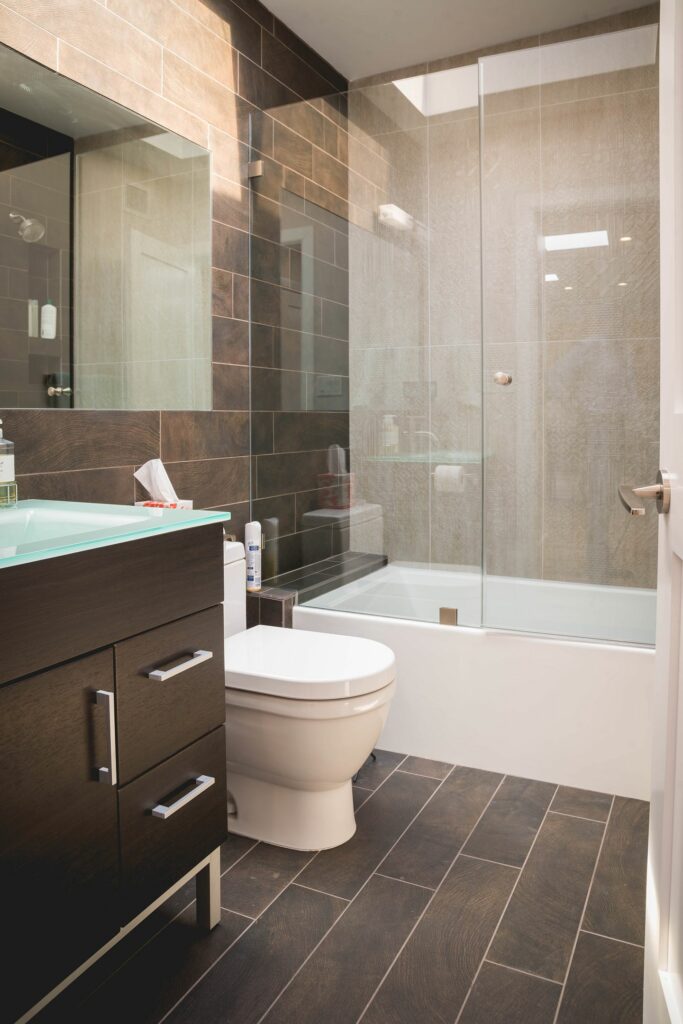 Modern bathroom interior with glass shower and wooden tile flooring.
