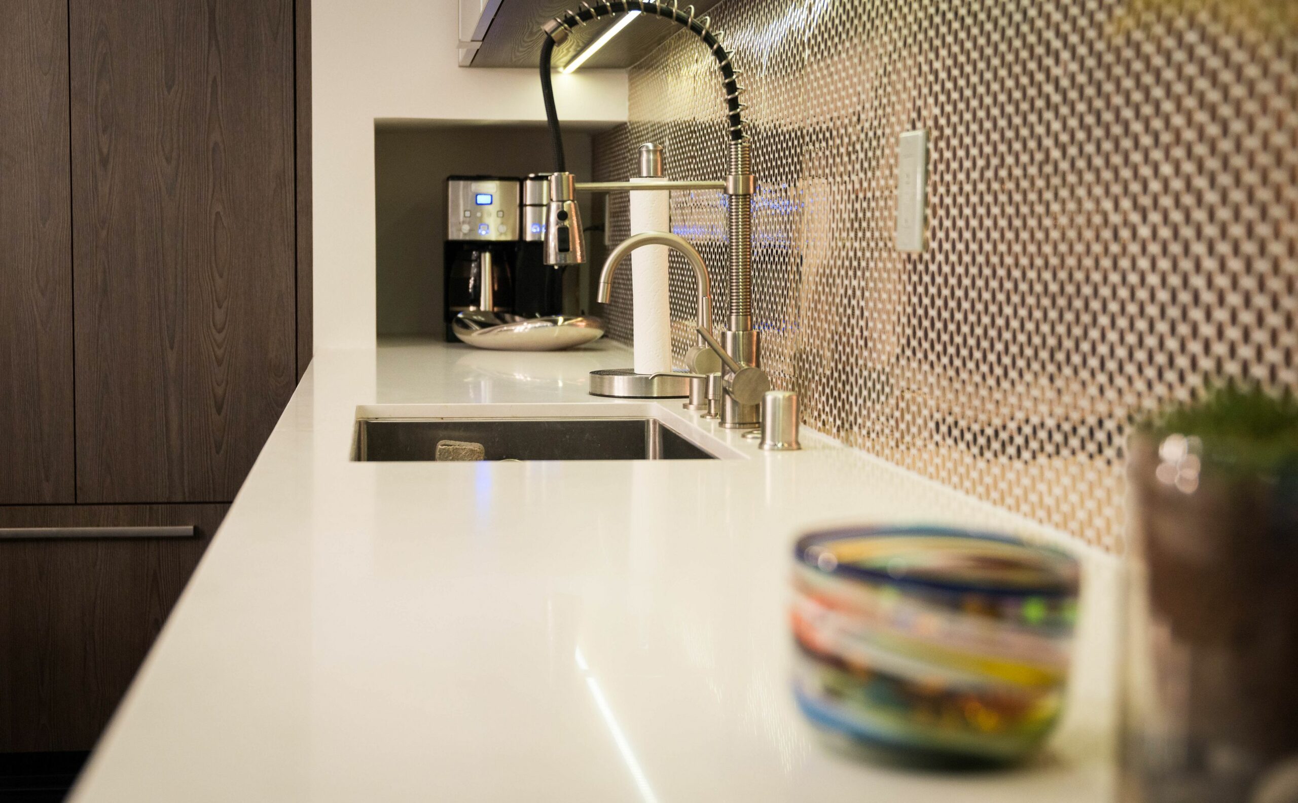 Modern kitchen interior with mosaic backsplash and stainless faucet.
