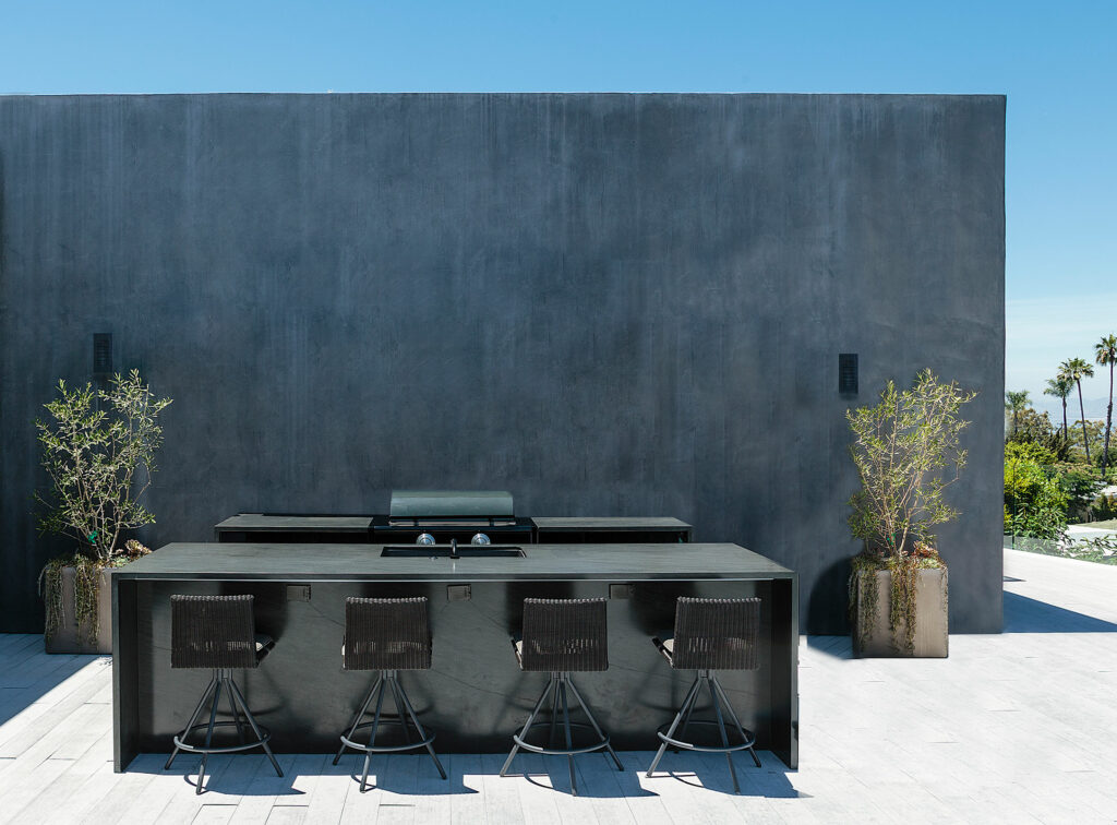 Modern outdoor kitchen with bar stools and concrete wall.
