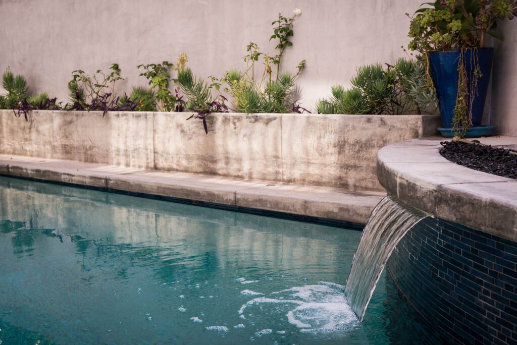 Tranquil backyard pool with waterfall and potted plants.
