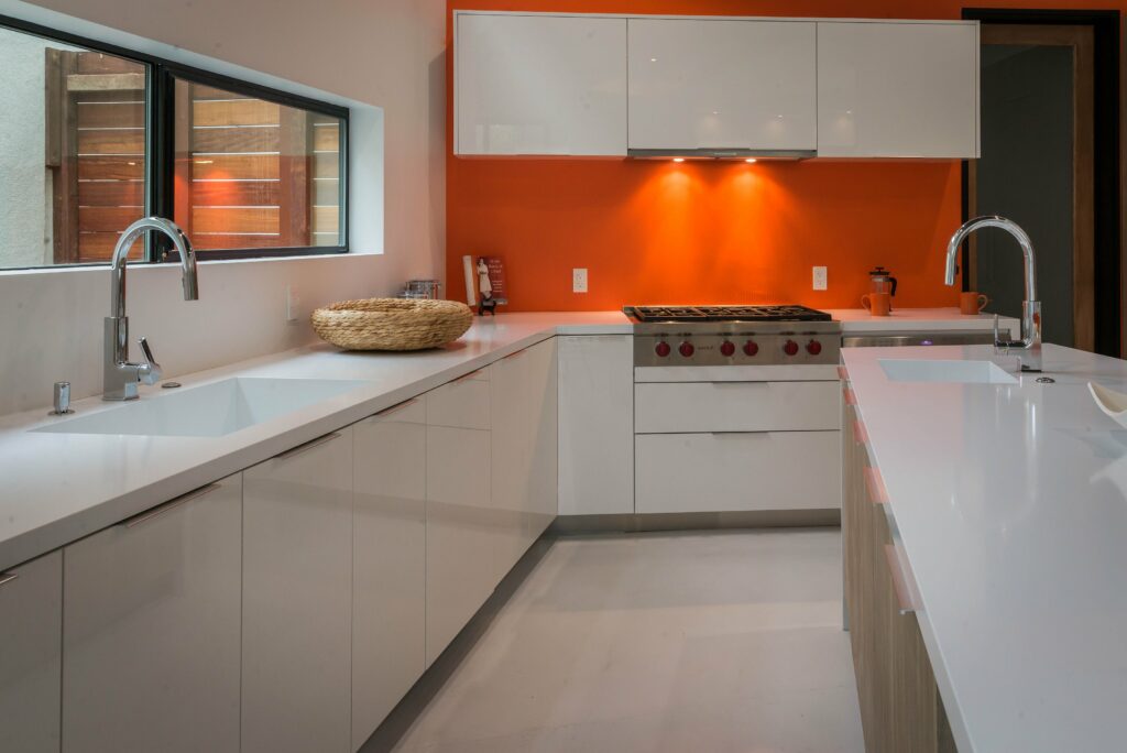 Modern kitchen with orange walls and white cabinets.