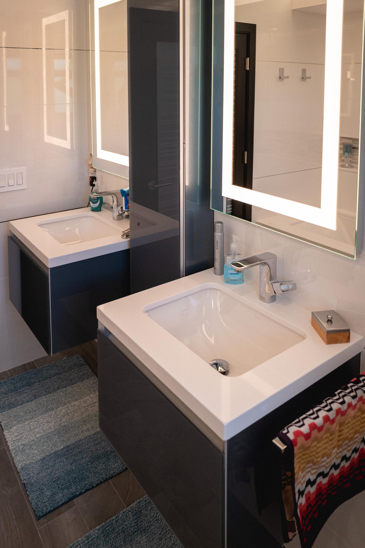 Modern bathroom with illuminated mirrors and double sinks.