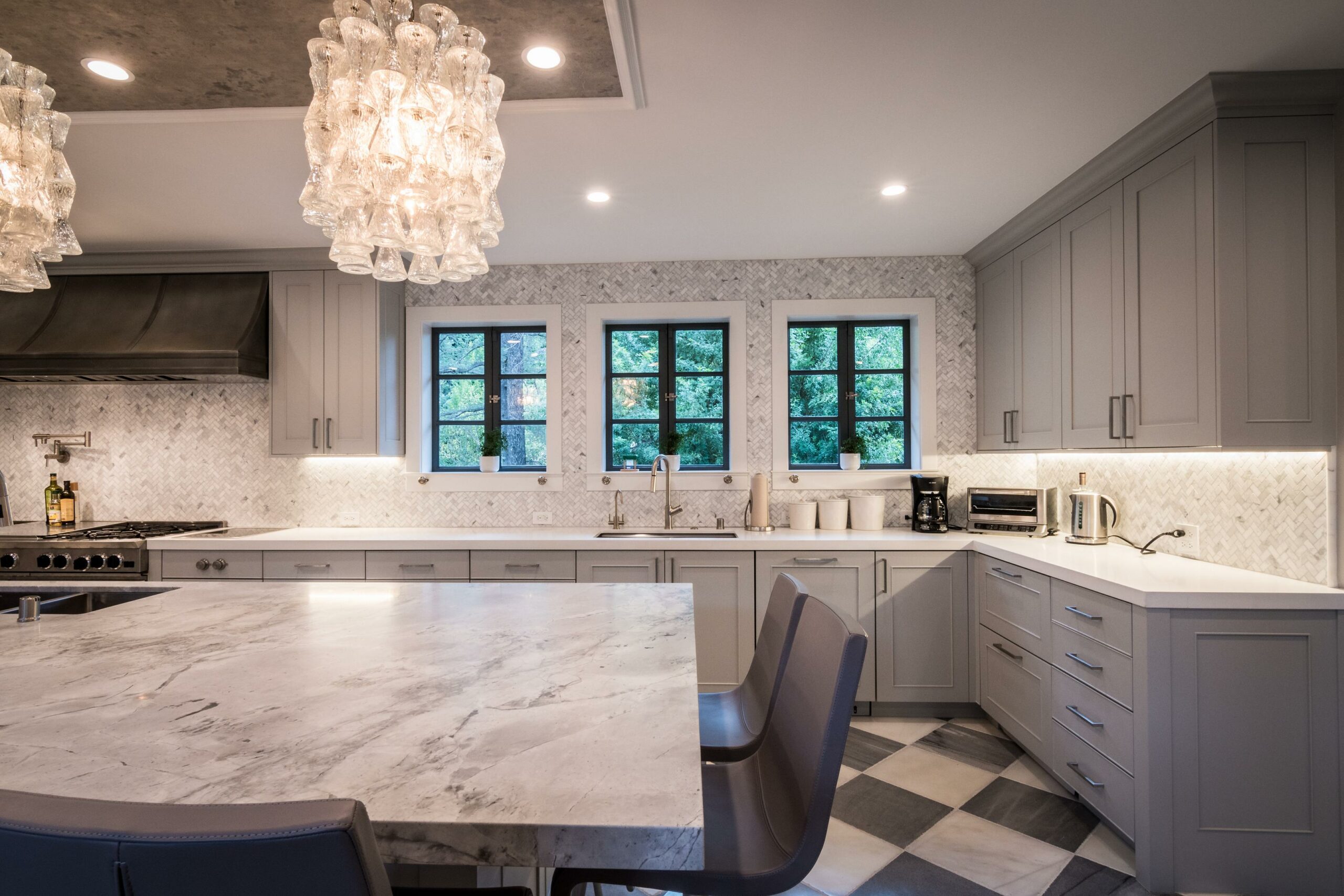 Elegant modern kitchen with marble countertops and chandelier.