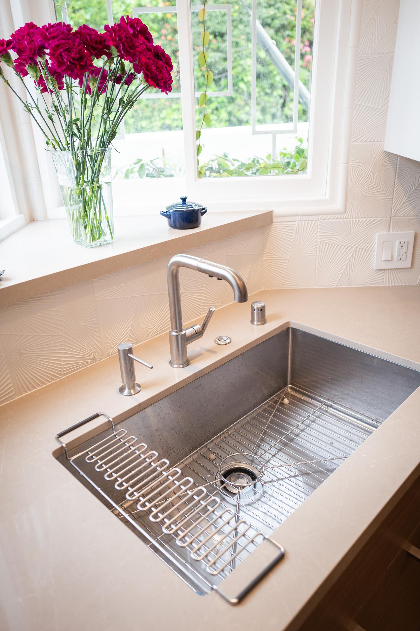 Modern kitchen sink with geometric backsplash and flowers.