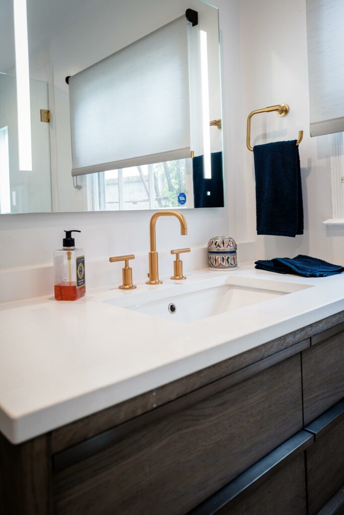 Modern bathroom sink with gold faucet and blue towels.