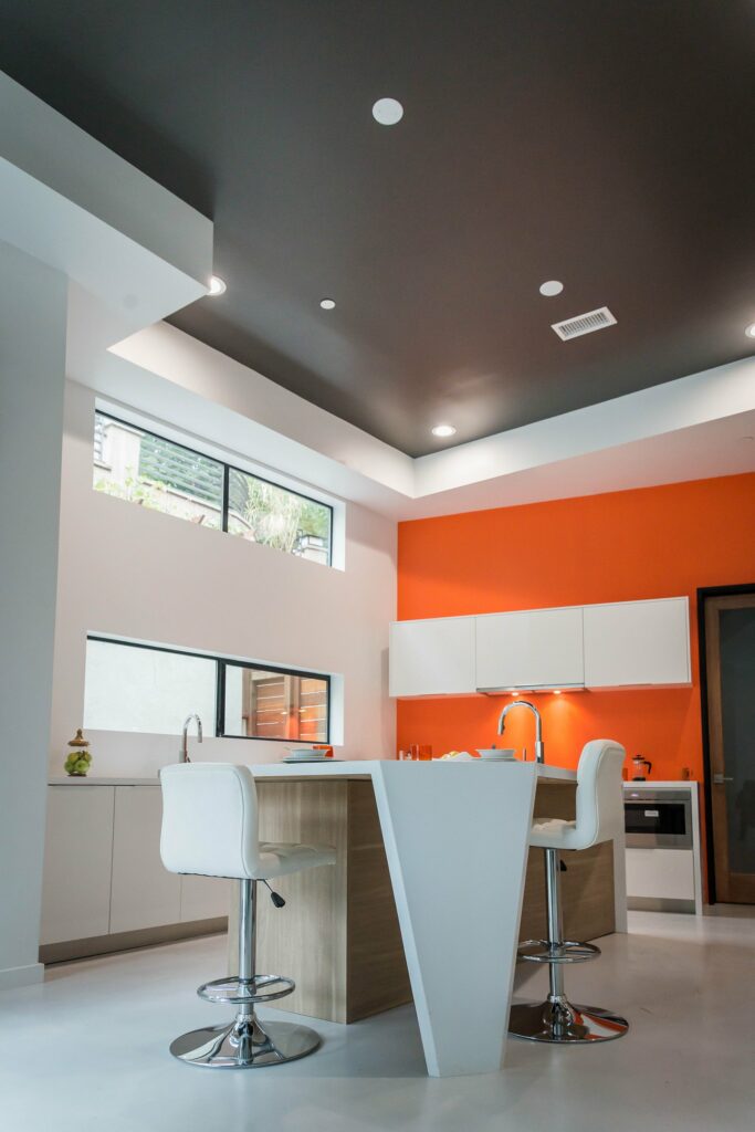 Modern kitchen with orange accent wall and bar stools.