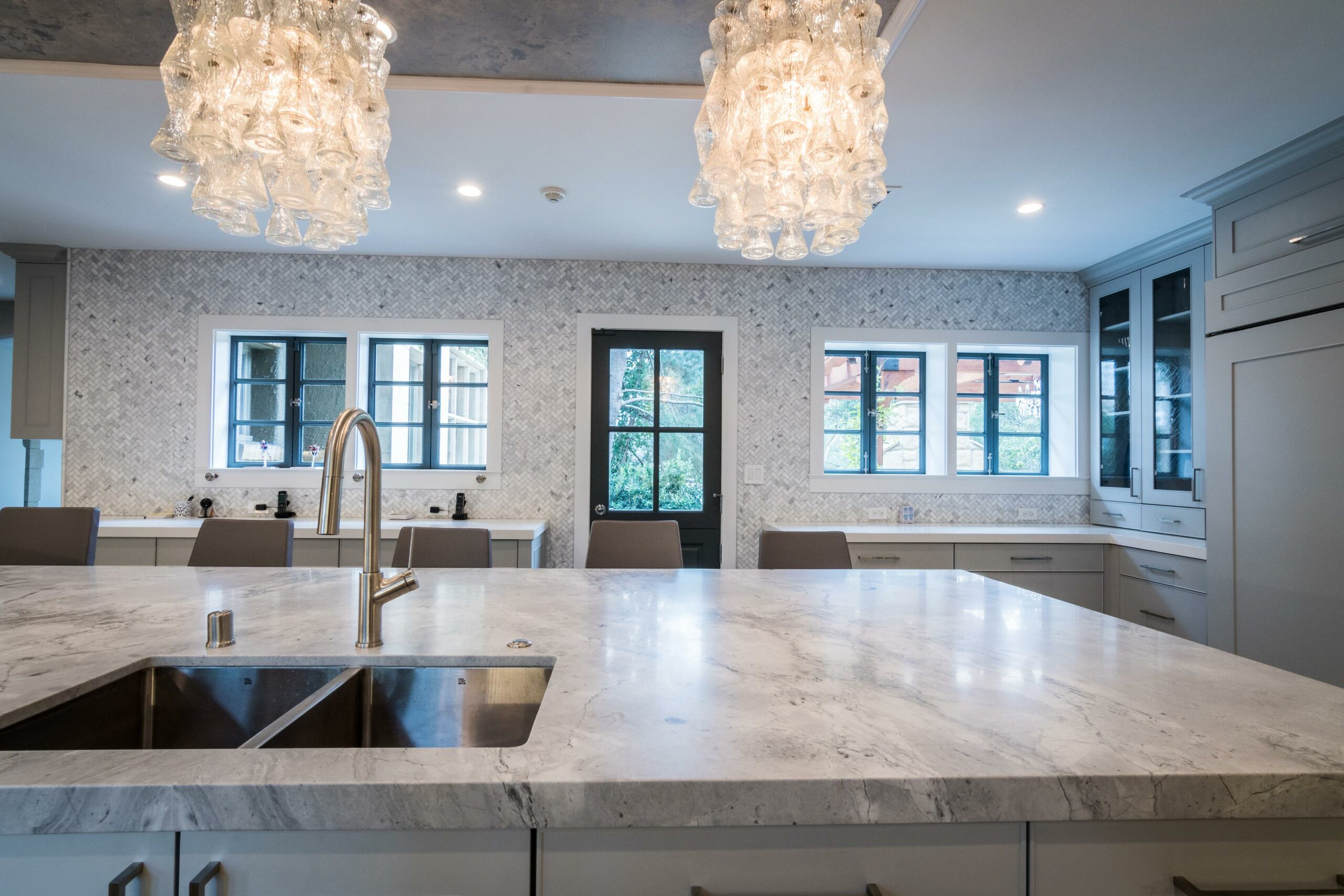 Modern kitchen with marble countertops and chandelier.