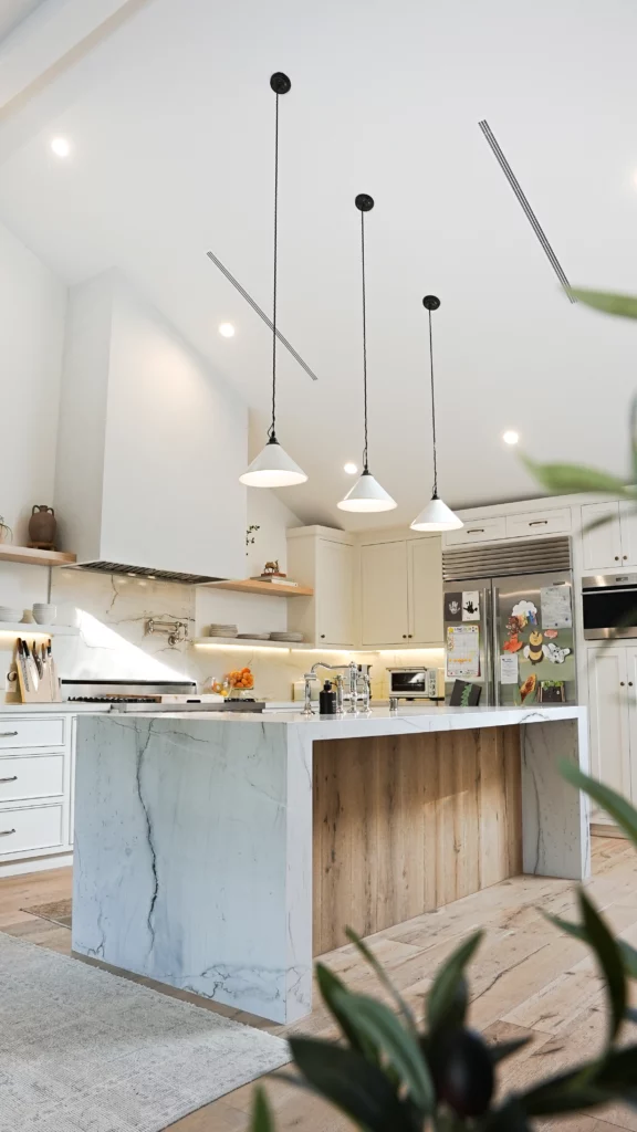 Modern kitchen interior with marble island and pendant lights.